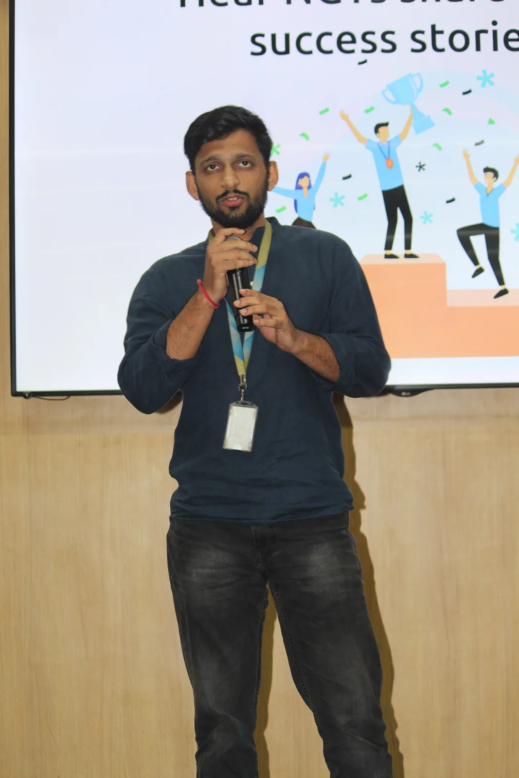 Harshit speaking into a microphone in front of a presentation slide reading "hear NGTs share success stories"
